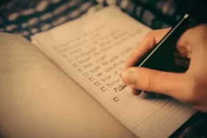 Dłoń trzymająca długopis nad zeszytem z checklistą rekrutacyjną.